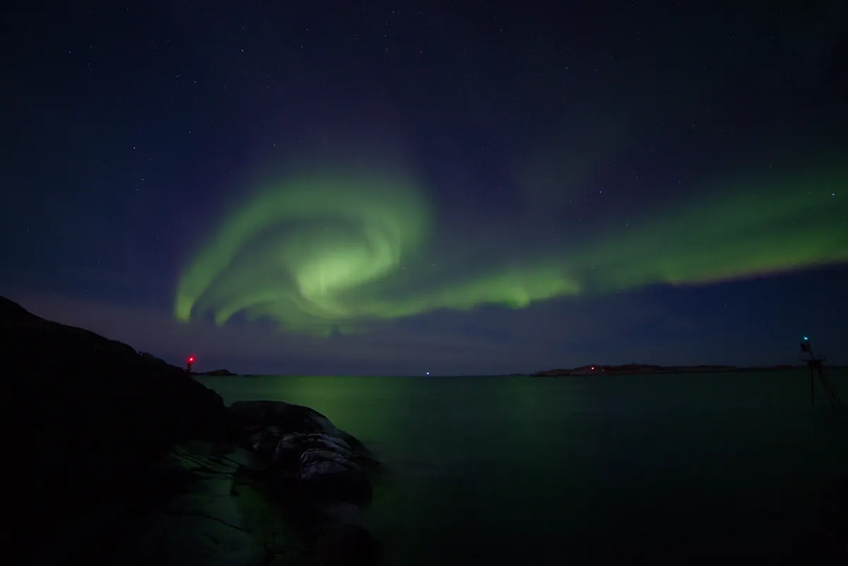Dancing green aurora borealis northern lights in Tromsø night sky over snowy Arctic mountains