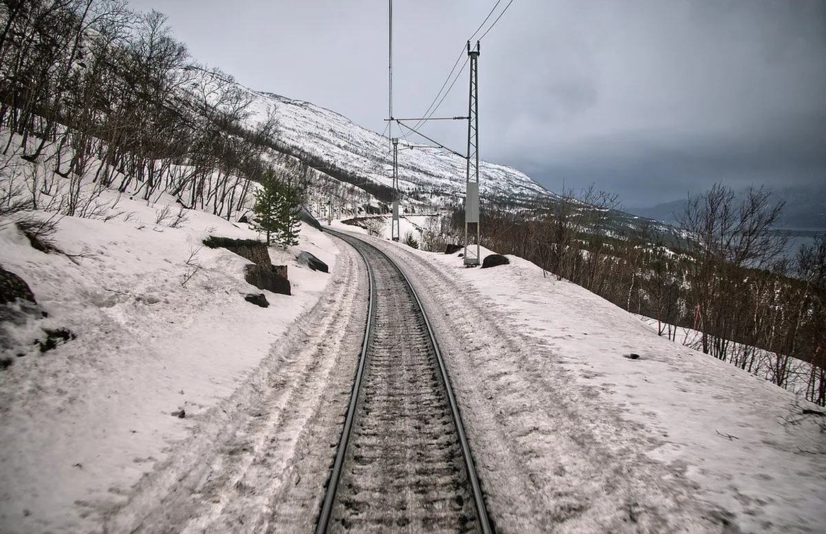 Train traveling through snowy Arctic landscape with mountain peaks, Ofoten Railway to Narvik