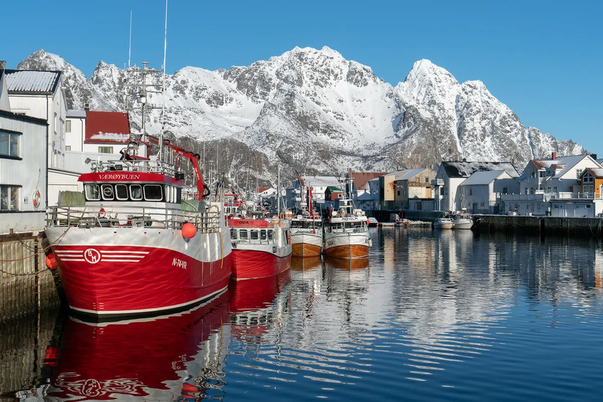 Ice fishing on a frozen Tromsø fjord with Arctic mountains in the distance, angler using jigging rod
