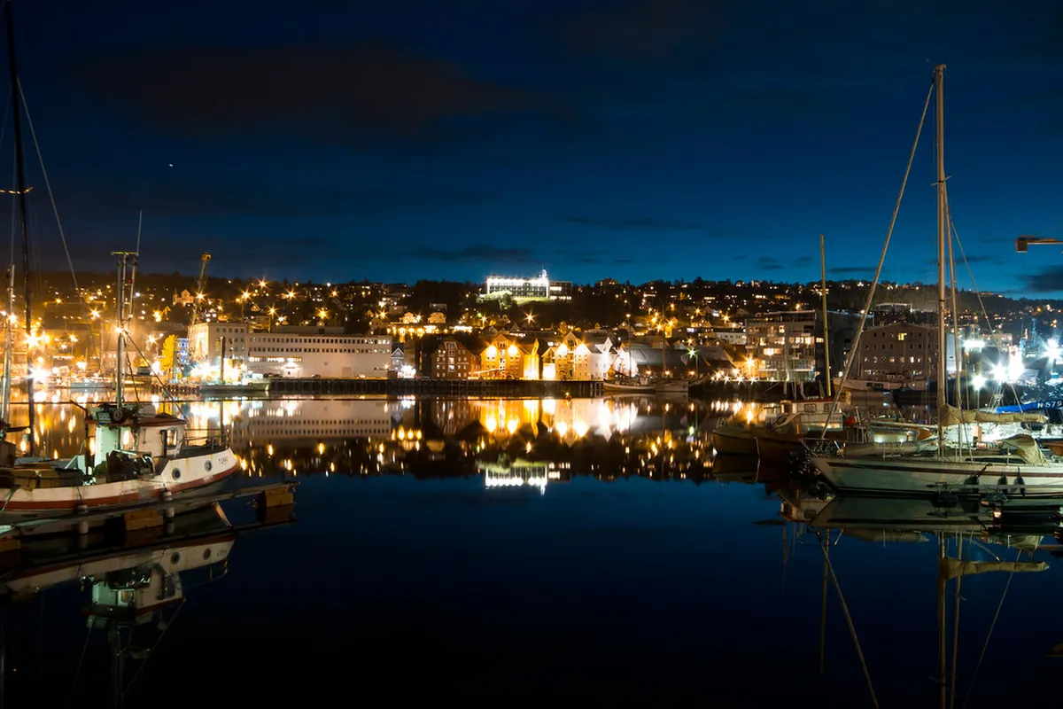 Tromsø harbour at midnight with boats docked and mountains glowing in golden midnight sun light