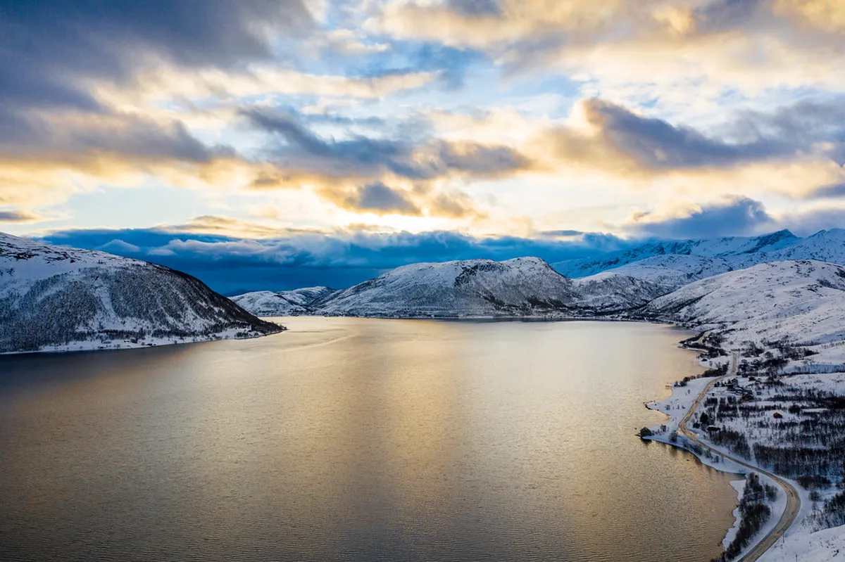 Tromsø fjord with snow-covered mountains reflecting in dark winter water, ideal for Northern Lights viewing locations
