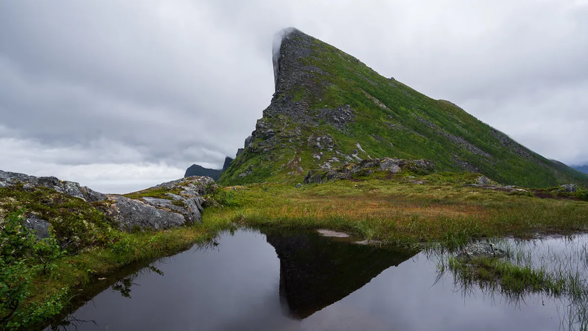 Okshornan granite peaks rising jagged above Ersfjord in Senja with Arctic waters and wooden viewpoint platform below