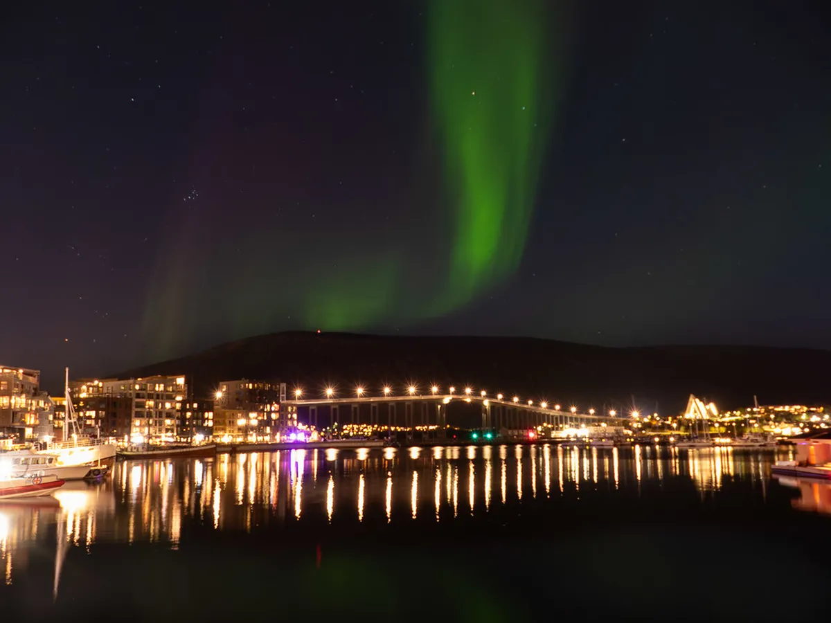Northern lights aurora borealis dancing over Tromsø Arctic beach with snow and dark winter sky