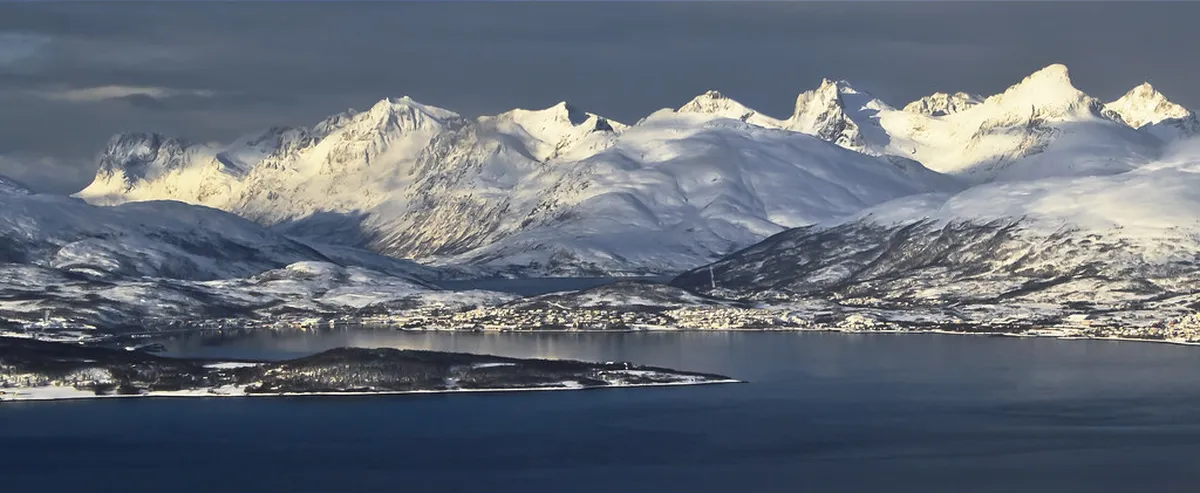Dramatic snow-covered mountain landscape of Tamok Valley in Tromsø, Norway with winding fjord beneath Arctic skies