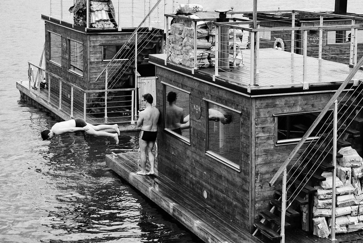 Person immersed in icy Arctic fjord waters beside wooden sauna platform in Tromsø during winter