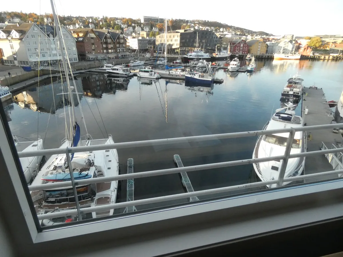 Wooden floating sauna structure docked in Tromsø harbor with fjord and snow-covered mountains in background