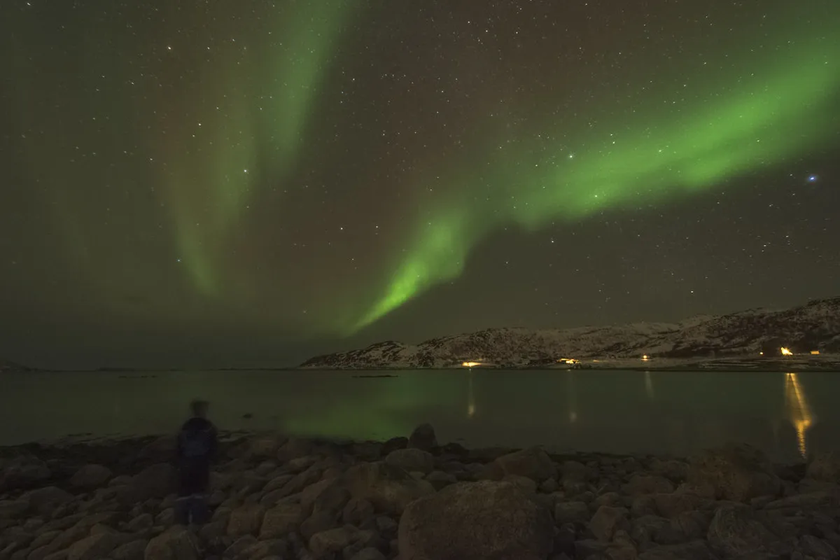 Aurora borealis dancing across a starlit Arctic sky over Tromsø fjord, with silhouetted mountains in the foreground